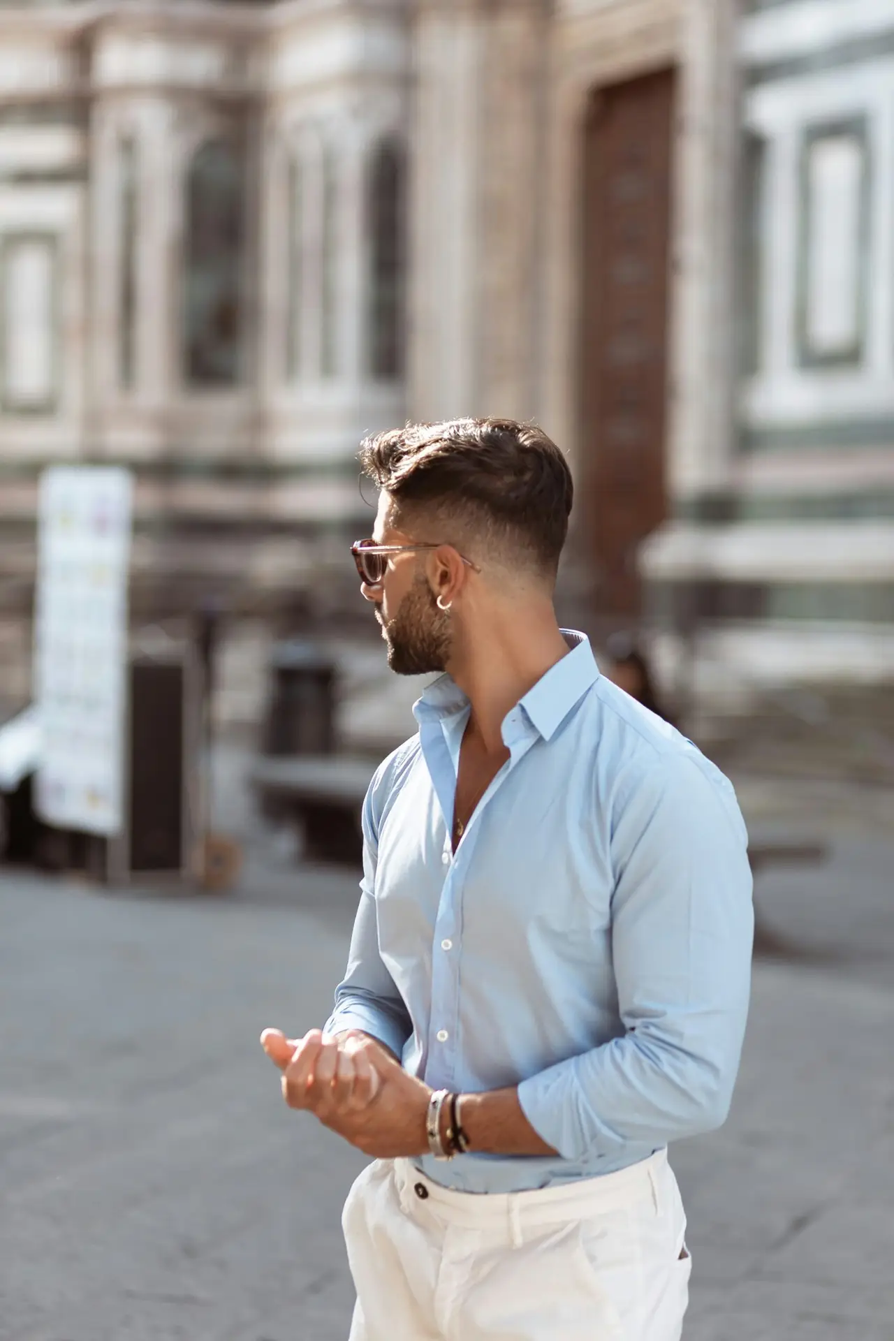 Hombre con gafas posando de manera directa contra la cámara, usando prendas básicas imprescindibles: camisa de vestir azul, unos chinos blancos y gafas de sol
