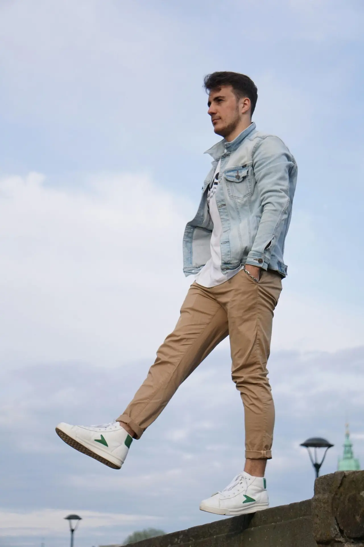 Hombre usando como prendas básicas imprescindibles: una chaqueta de mezclilla, camiseta blanca, chinos marrones y zapatos de talón alto blanco